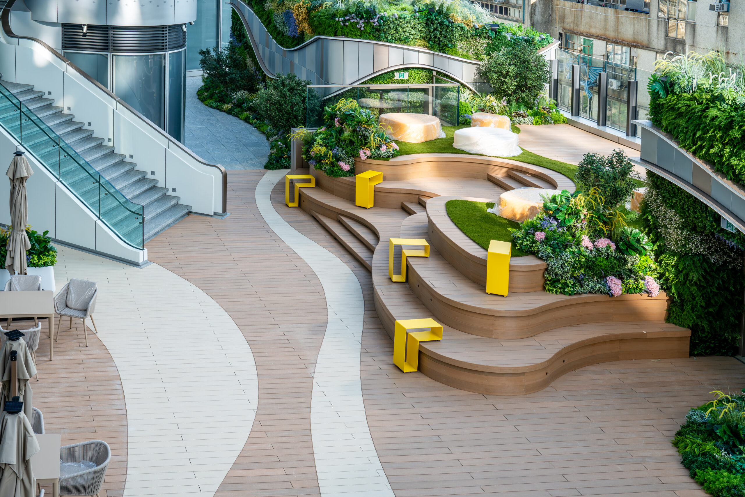 Curved terraced decking steps doubling as seating, with a glass-sided staircase to one side and planting between the levels