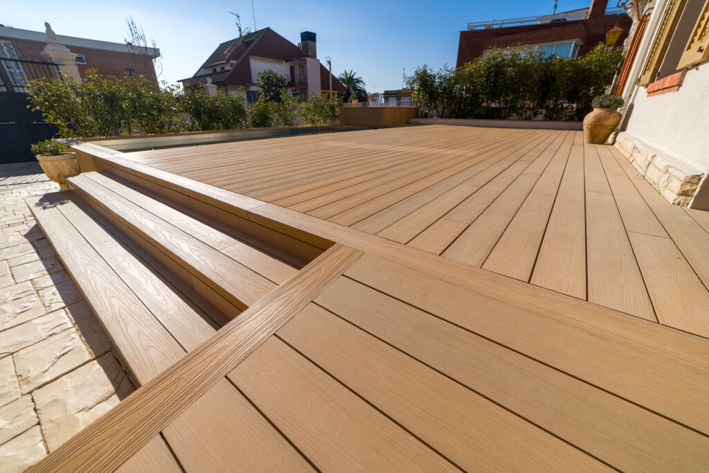 Light composite deck with wide low steps down to a stone patio on a residential terrace, no railing at the edge