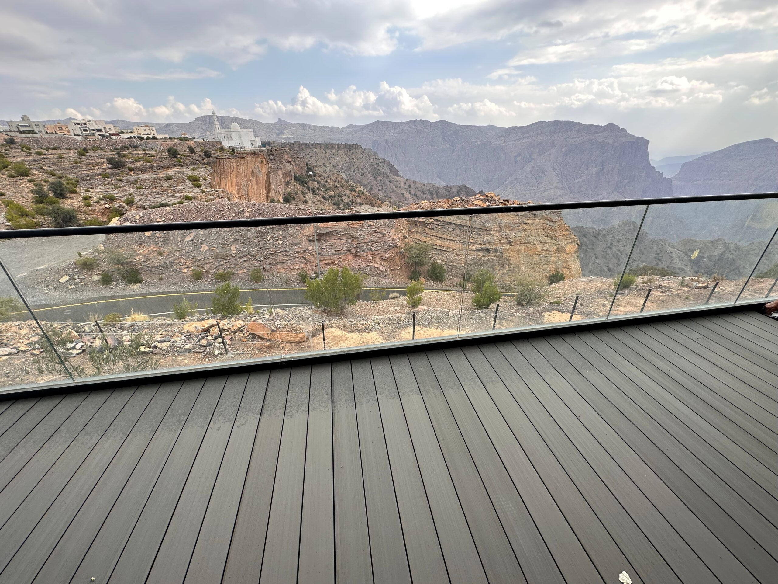 Small terrace in dark grey composite decking with a frameless glass balustrade, overlooking a canyon
